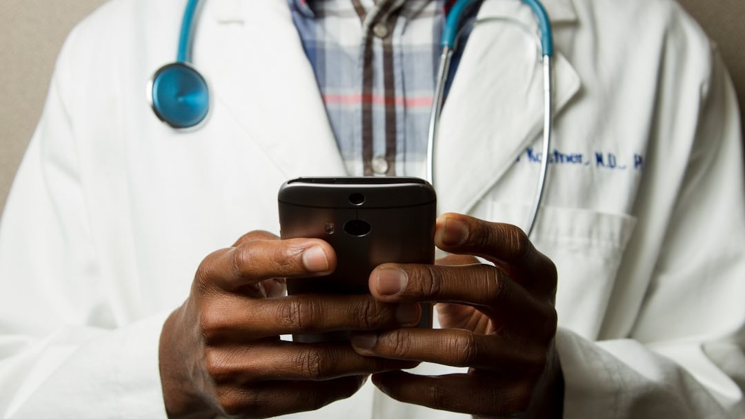 person wearing lavatory gown with green stethoscope on neck using phone while standing